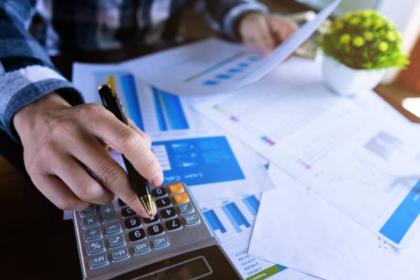 Close up businessman using calculator and reading paper document about business data, accountancy document, ESG Reporting.